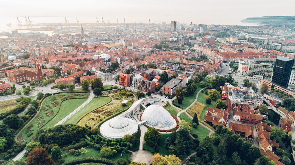 Drone footage of large white buildings that look like bubbles surrounded by large green areas and orange brick buildings