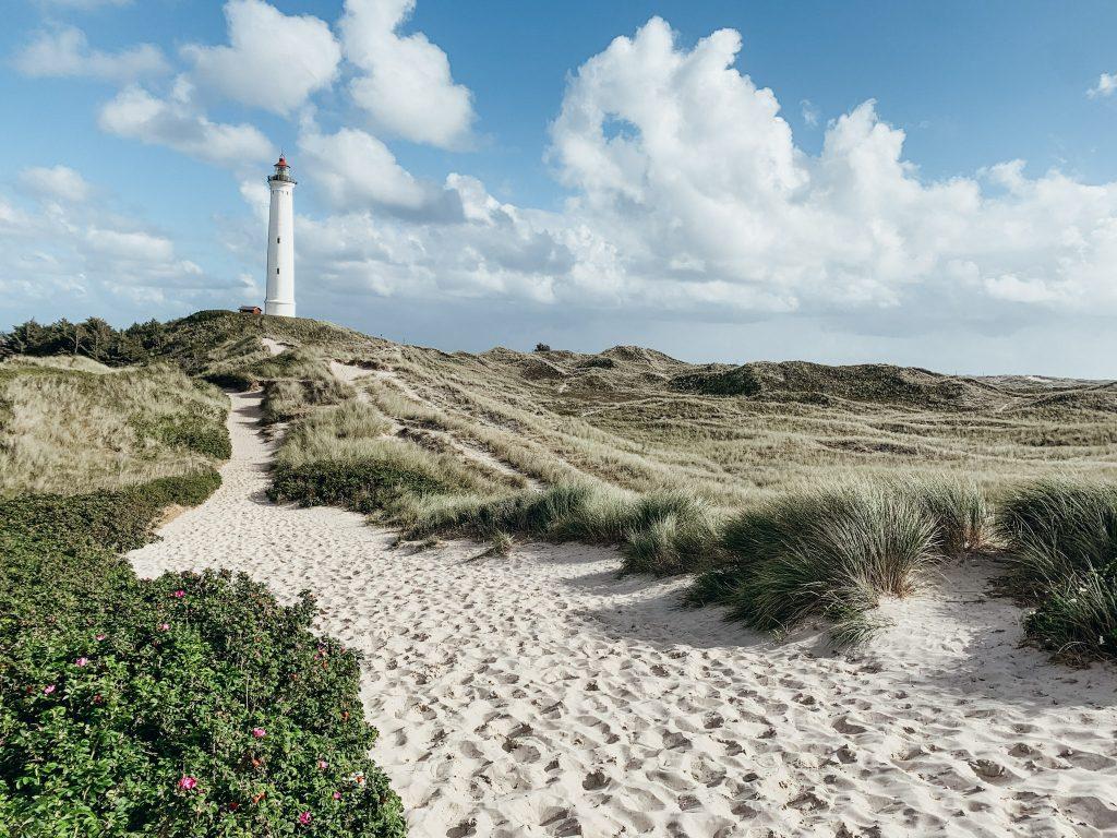 Sand path over grassy dunes to tall white lighthouse